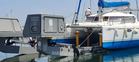 Amphibious craft with enclosed cabin and ramp deployed alongside white and blue motor yacht at marina