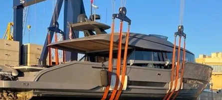 Fixed gantry crane with orange lifting spreader hoisting cream and navy sport cruiser above Mediterranean harbor