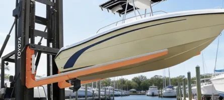 Yellow and blue self-propelled boat forklifts positioning cream and blue cabin cruiser on transport frame