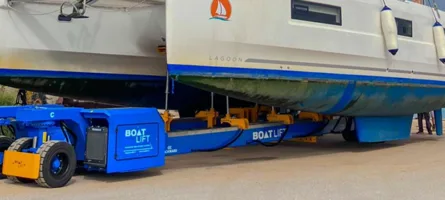 Blue self-propelled boat trailer with yellow forklifts and cradle securing cream cabin cruiser on coastal road