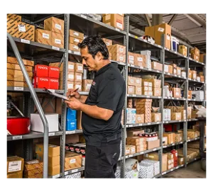 Technician checking inventory on industrial shelving stocked with labeled boxes and parts in warehouse facility